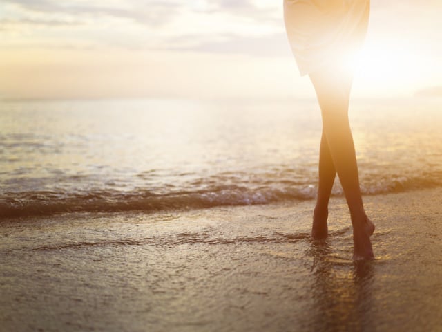 woman walks along the ocean at sunset